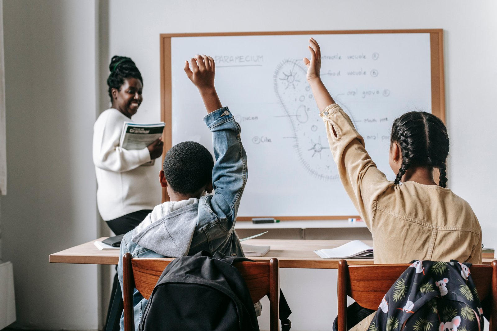 Docente frente a estudiantes con las manos levantadas